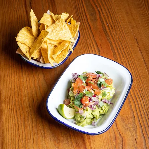 Guacamole con nachos y pico de gallo de Porco Dio servido en mesa de madera