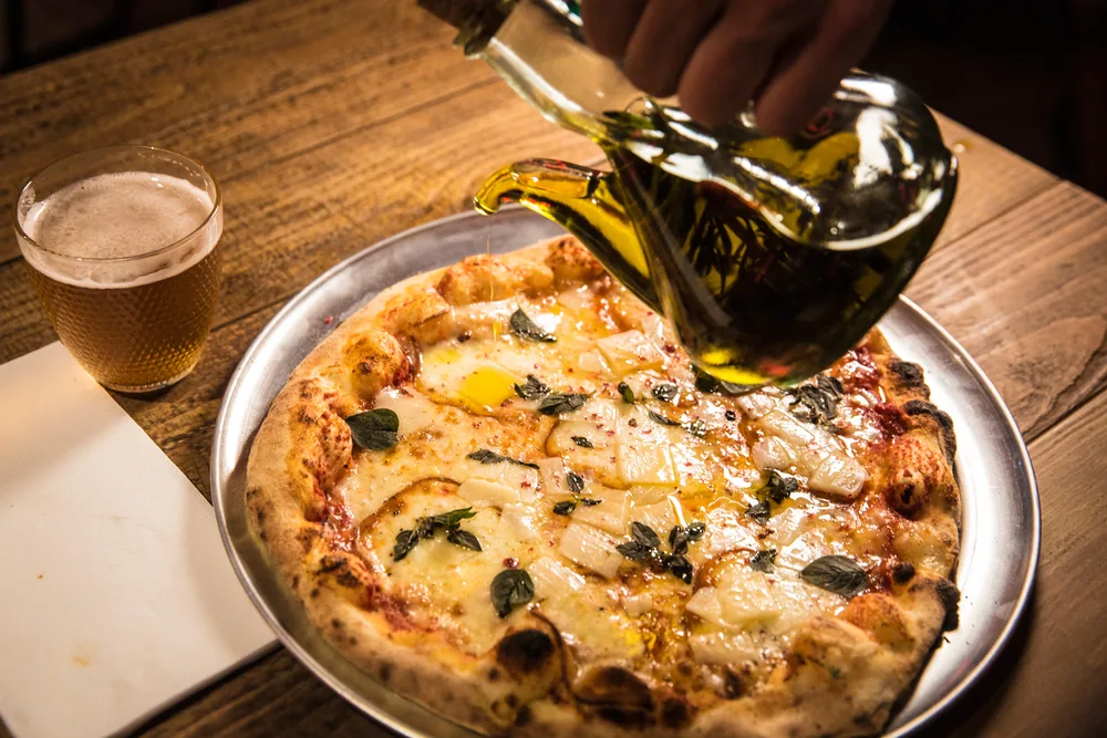 Chorro de aceite de oliva sobre una pizza napolitana recién horneada en Porco Dio, con una cerveza al lado