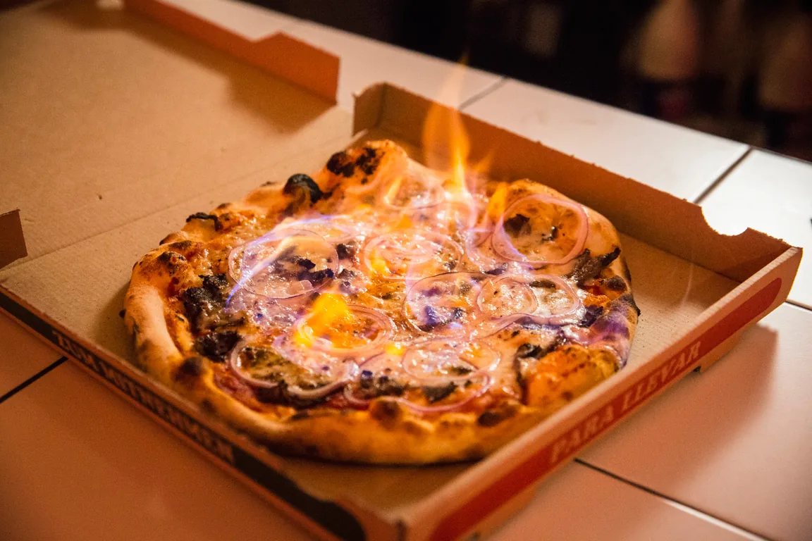 Pizza de Porco Dio flambeada en su caja con llamas azules y naranjas